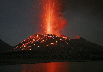 Nächtlicher Ausbruch des Vulkans Tavurvur mit Lavafontäne, gespiegelt im Wasser